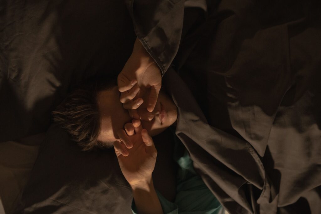 A man covering his eyes with a pillow in bed, suggesting insomnia or relaxation.